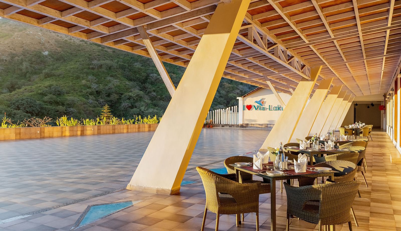 An outdoor dining area with tables and chairs under a covered patio, overlooking a landscape - Via Lakhela Resort & Spa, Kumbhalgarh