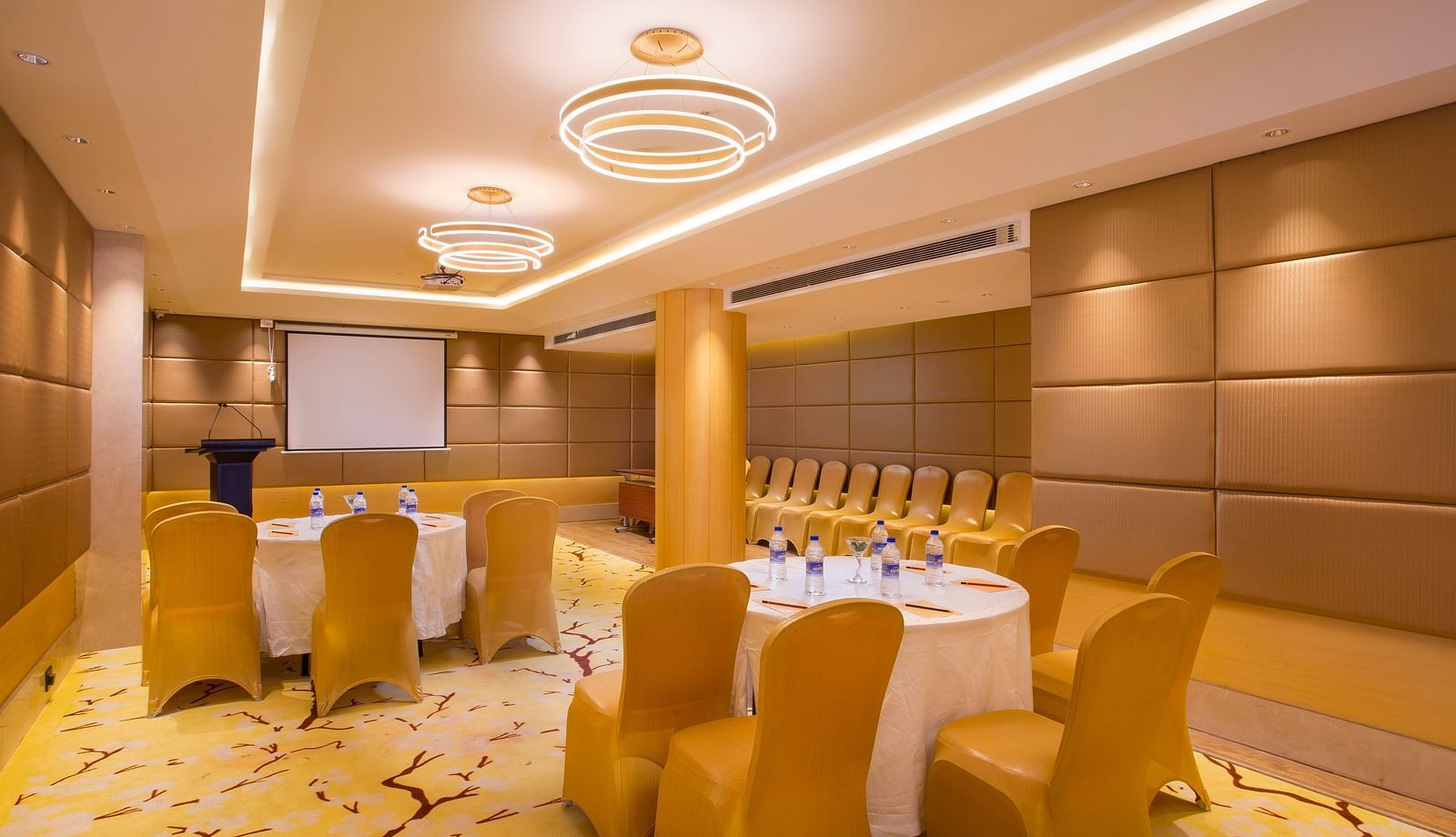a conference hall with clusters of tables and chairs spread across the hall, where all the chairs are facing the projector - Hotel Fountain Tree By TGI - JP Nagar, Bangalore