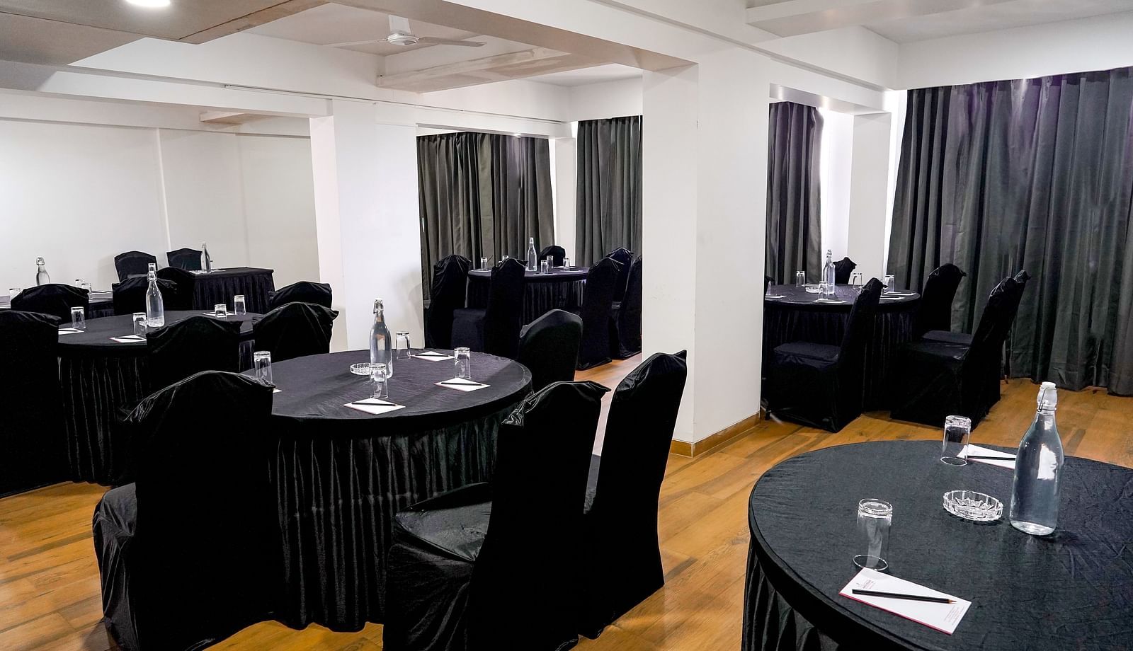 A conference room corner with black-draped tables and wooden flooring - TGI Ameya Grand, Goa