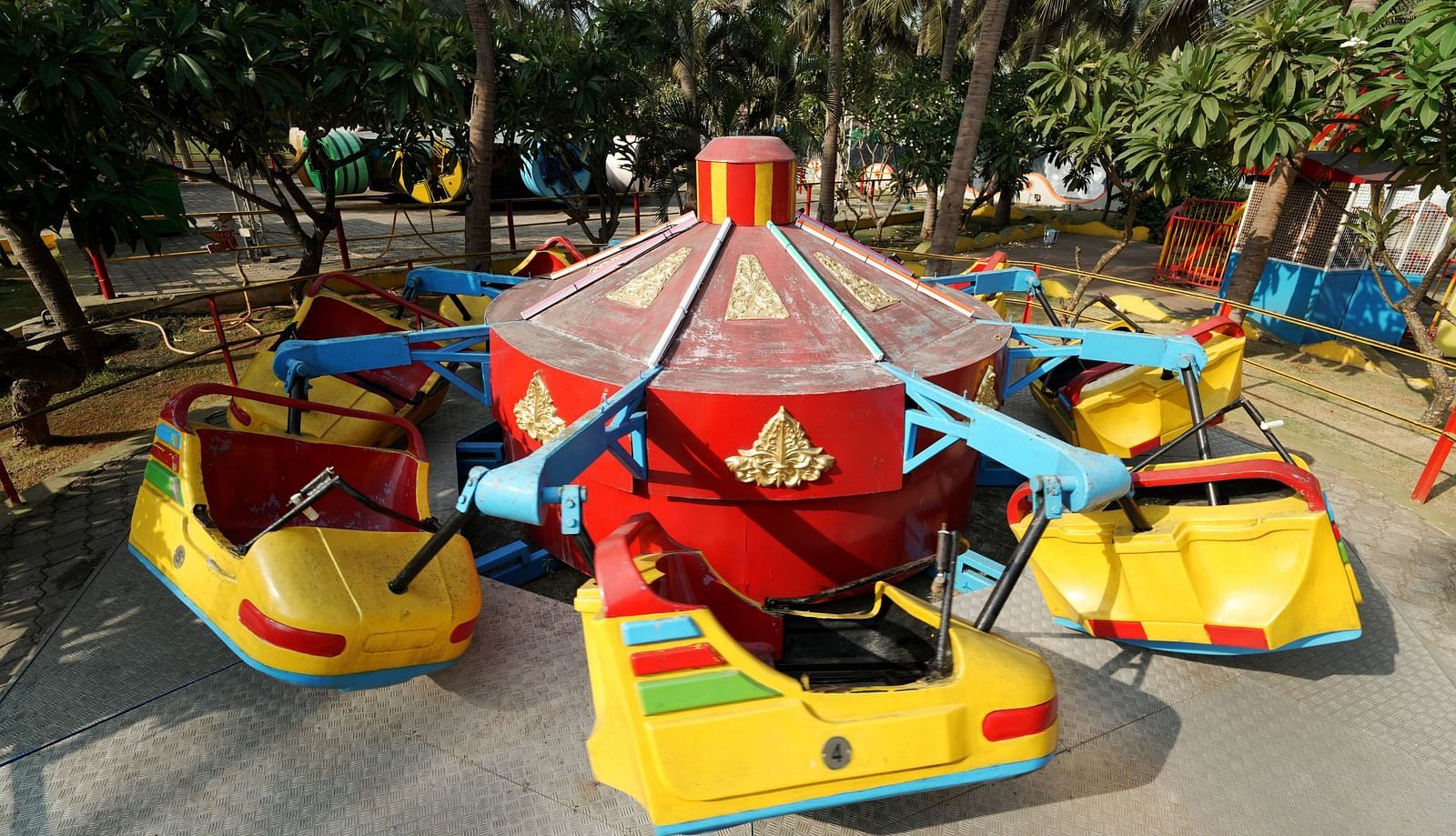 A vibrant carousel ride with yellow and red cars in an outdoor amusement park, surrounded by trees.