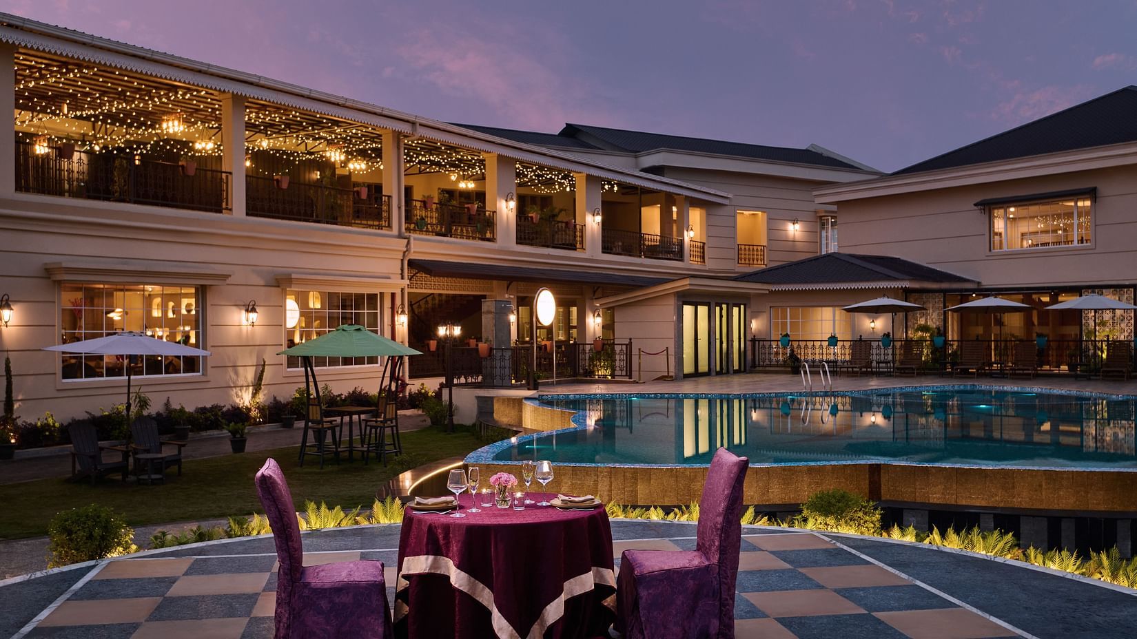 Outdoor swimming pool at Voyage The Solitaire Bliss, set against a stunning sunset sky, with the hotel building beautifully lit by elegant lighting in the background