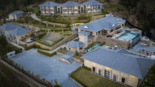 High-angle view of the Royal Tulip Shivapuri National Park - Kathmandu resort complex, showing multi-story buildings, a pool, and tiered stone landscaping.
