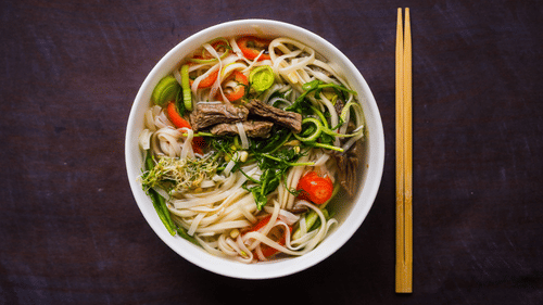 a bowl of noodle soup garnished with vegetables with a chopstick on the side