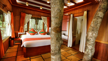 Room with a bed and tree trunks protruding out of the floor at Vythiri Resort, Wayanad