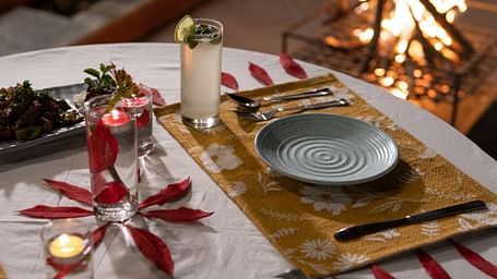 A close-up view of a table neatly set with food and cutlery, with a campfire in the background at BluSalzz Villas - The Green Roof, Bhimtal.
