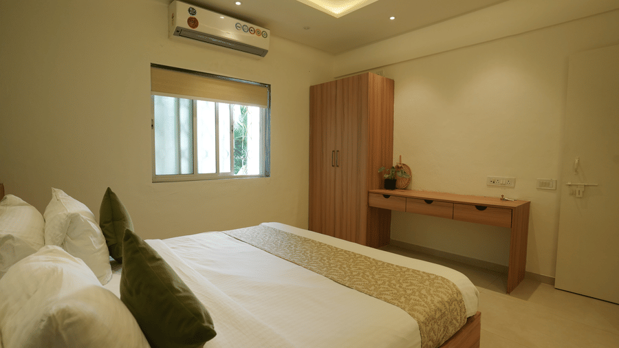 A bedroom with a king size bed, a wooden wardrobe, a desk, and a window at Oceanature Resort, Alibaug.