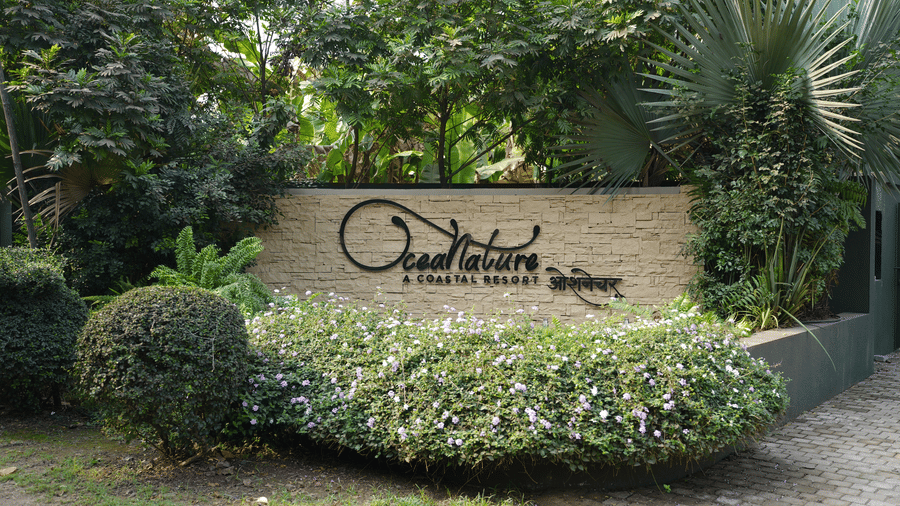An outdoor stone sign surrounded by bushes and trees marks the entrance to Oceanature Resort, Alibaug.