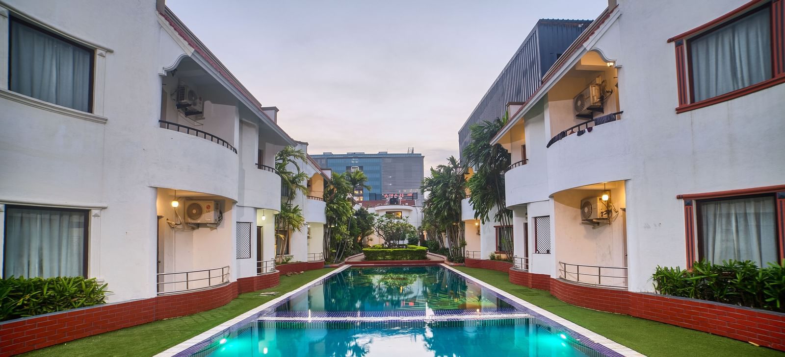 A symmetrical view of Ilara Hotels & Spa, OMR, Chennai with red roofs, flanking a long, narrow swimming pool or water feature, bathed in daylight.