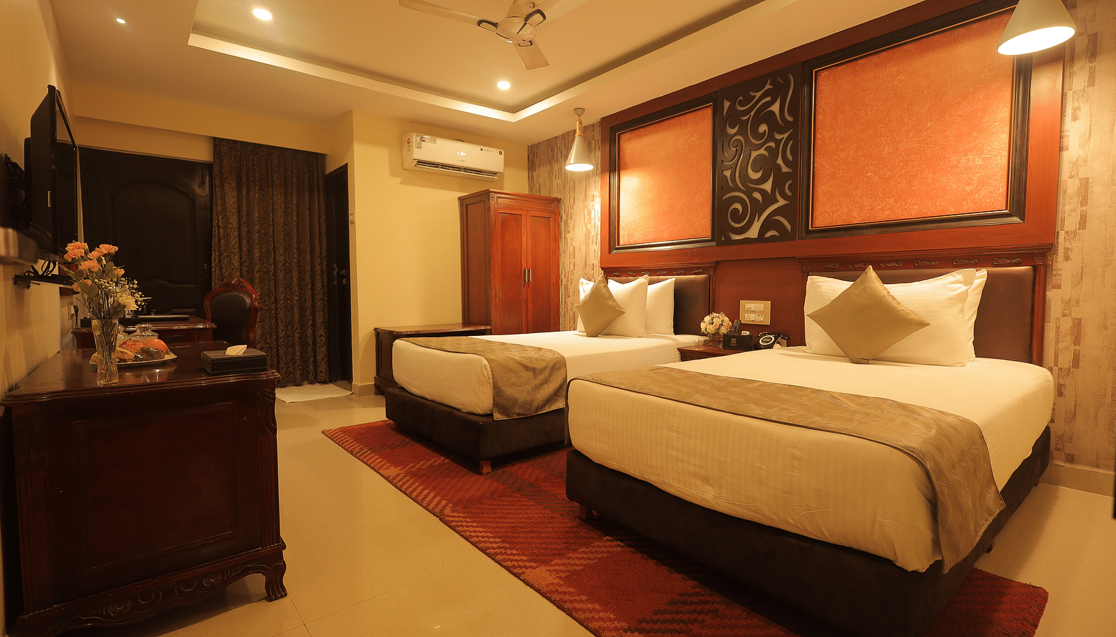 An image of a twin beds with bedside table, a set of table and chairs, flat TV screen, and AC - Sathyam Grand Resort