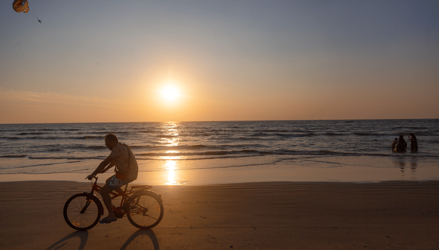 a person cycling on the beach with the sun setting in the background - Caravela Beach Resort Goa