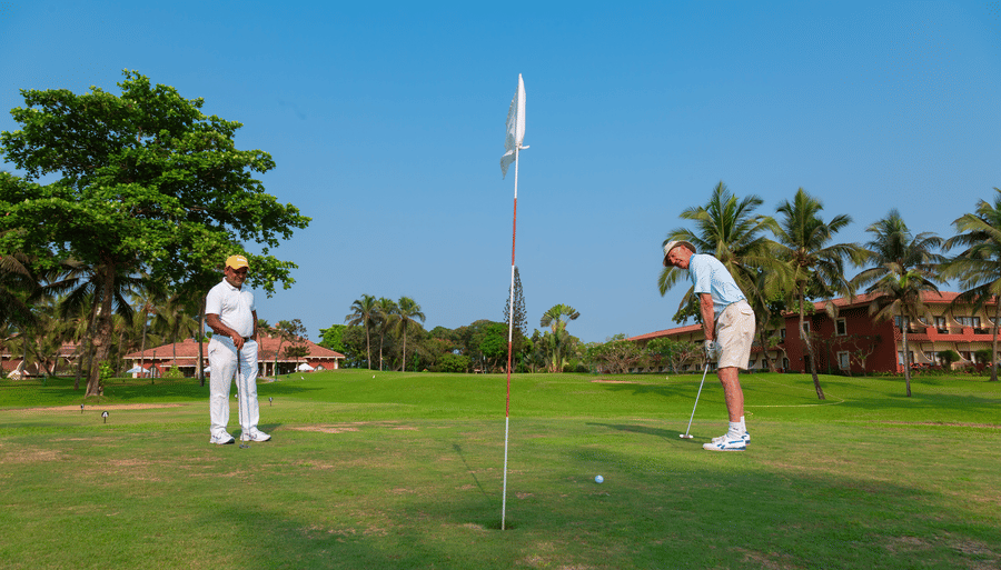 two people playing golf on the golf course with trees in the background - Caravela Beach Resort Goa