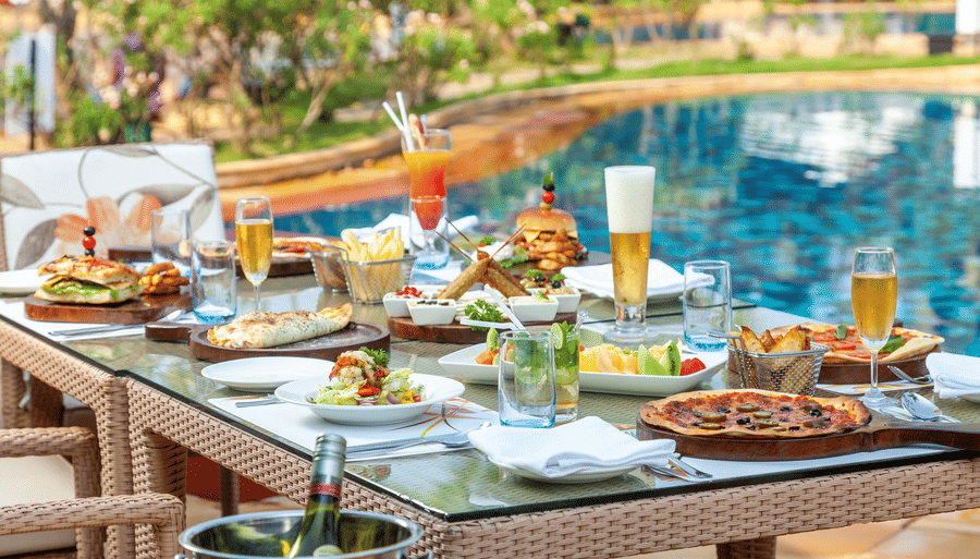 many types of food items kept on the table in front of the swimming pool - Caravela Beach Resort Goa