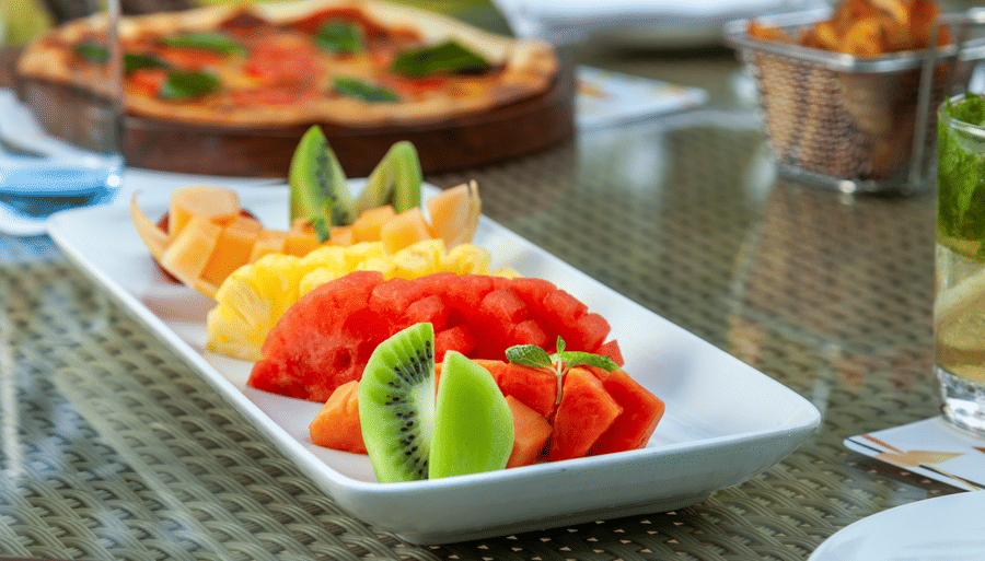 a fruit platter with a pizza in the background - Caravela Beach Resort Goa
