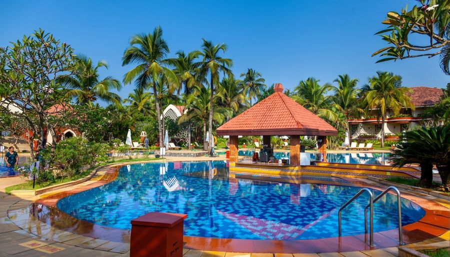 overview of the swimming pool with trees in the background - Caravela Beach Resort Goa