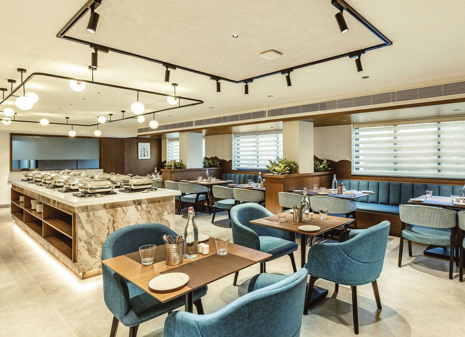 A wide shot of the restaurant at Mango Hill Central, Chennai, showing tables with blue chairs and a buffet area.