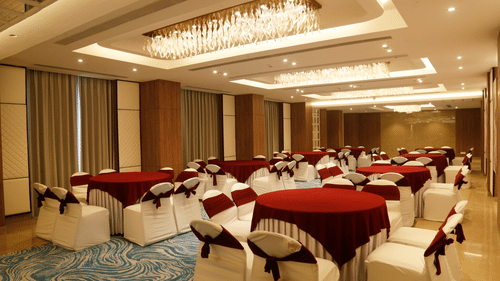 A banquet hall in Zirakpur with round tables, carpeted floors, and warm lighting - Tulip Inn, Zirakpur