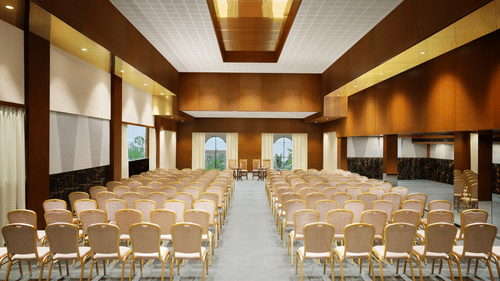 A well-lit event hall with chairs arranged neatly facing a central stage, featuring modern wooden interiors, windows offering natural light, and a sleek, polished floor - Uday Backwater Resort