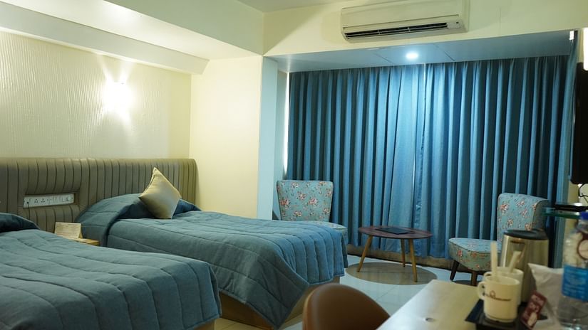 An image of a bedroom with twin beds, AC, table and chair, and two single sized sofa