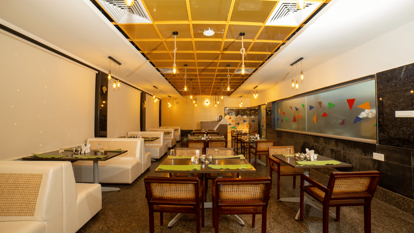 Looking down the length of the dining hall, showing repeated rows of tables, chairs, and white booths at Icon Express By Bhagini, Hoodi.