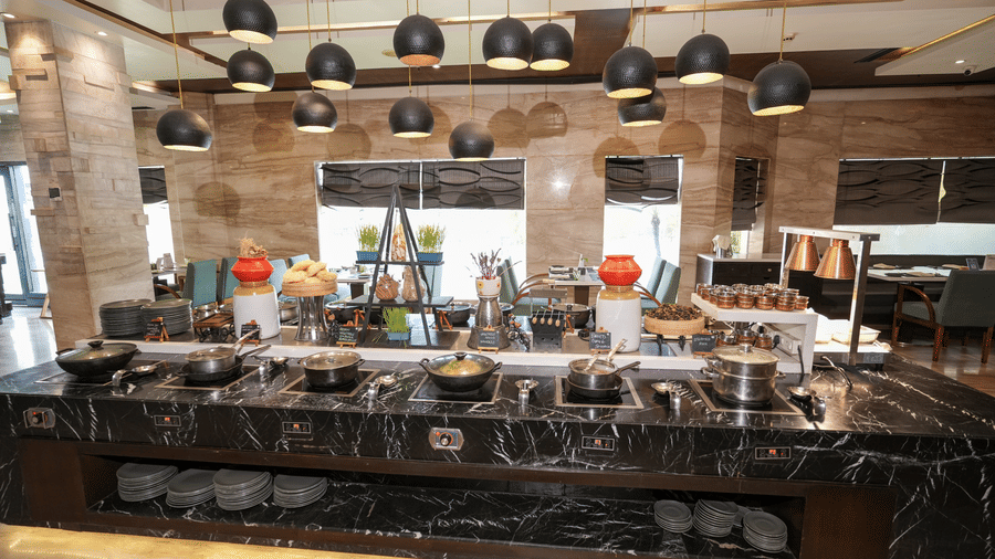 A buffet counter at Park Plaza Ludhiana featuring a dark marble surface with food displays hanging pendant lights and a stone textured wall backdrop in a warmly lit setting.