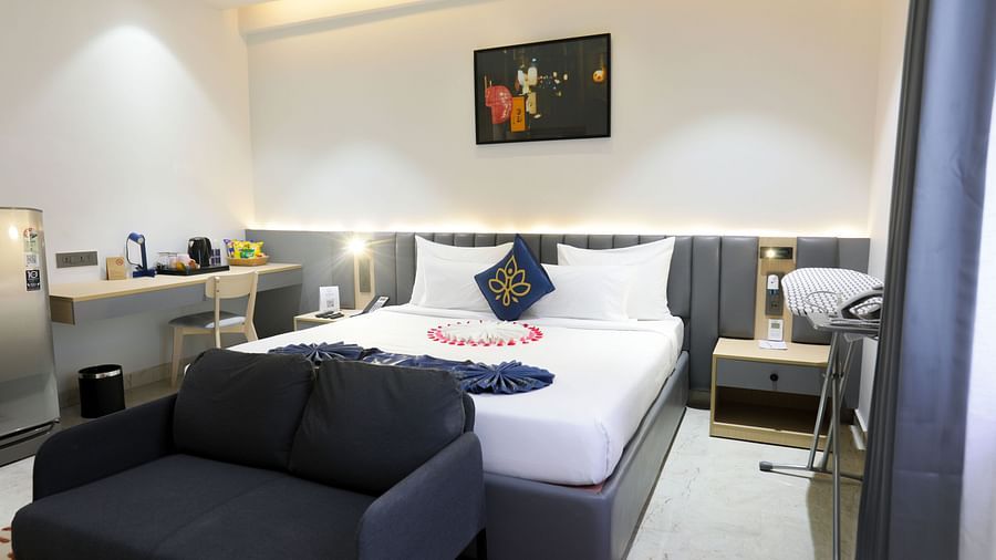 A room with king size bed, dark sofa, bedside table, framed art work on the wall and soft lighting at Hotel Kyzen HiTech City – Your Zenly Stay.