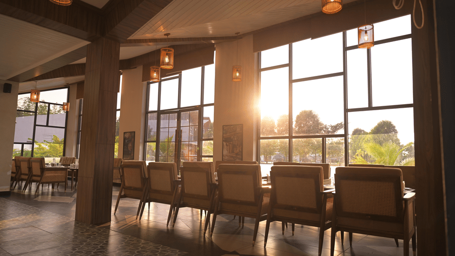 Indoor dining area with warm lighting and a sunset streaming through large windows at Hotel Sonar Bangla, Mayapur.