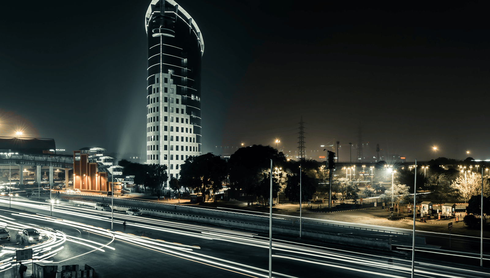 An overview of Gurgaon with a building, flyover and vehicles passing through in the night