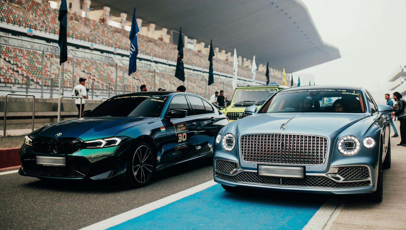 Cars lined up on Buddh International Circuit, with grandstands and flags in the background.