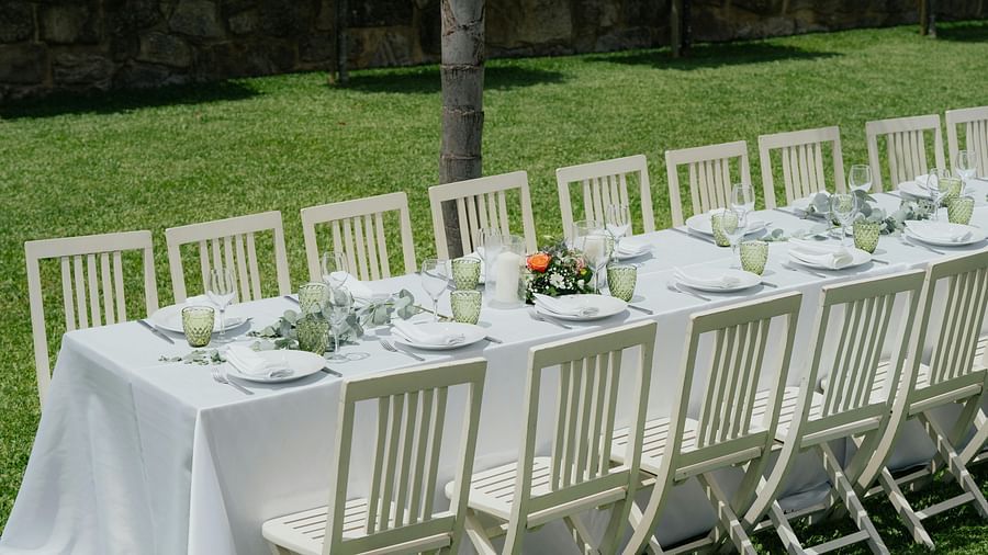 An image of a lawn where chairs and tables are lined up in order with cutlery and floral decoration