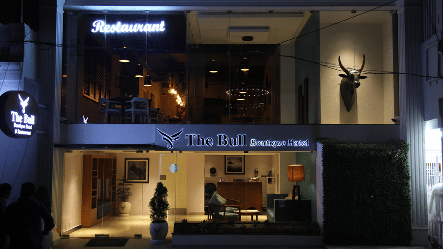 The modern exterior storefront of the hotel at night with bright signage and large glass windows at The Bull Boutique Hotel.