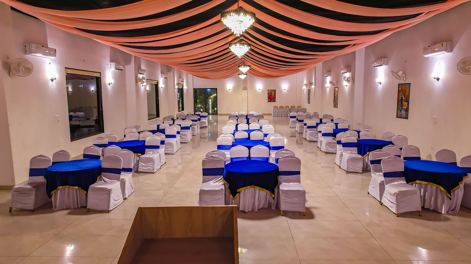 A long indoor dining hall at Vedikant Resorts The Mallard Corbett shows rows of tables and chairs beneath a decorated ceiling.