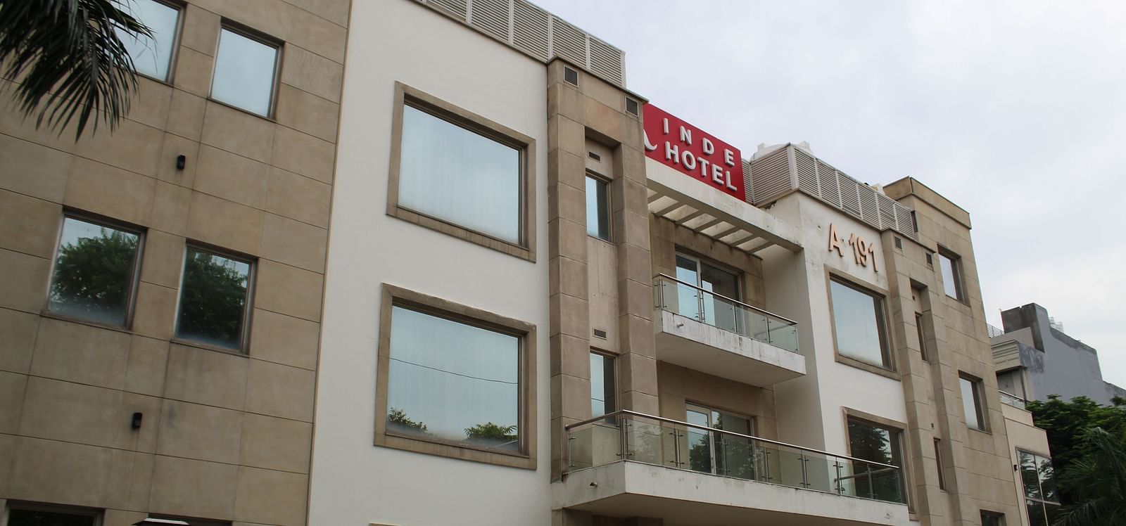 A facade image of Inde Hotels Vista Voods GUrgaon featuring a  triple storey building with huge windows and a board where the hotel name is mentioned