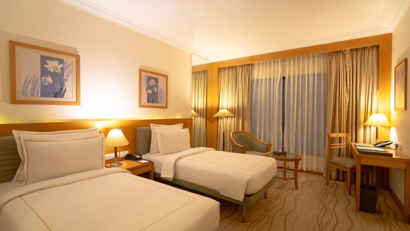Twin beds in this Accord Chrome hotel room, with nightstands, lamps, and framed pictures on the wall.