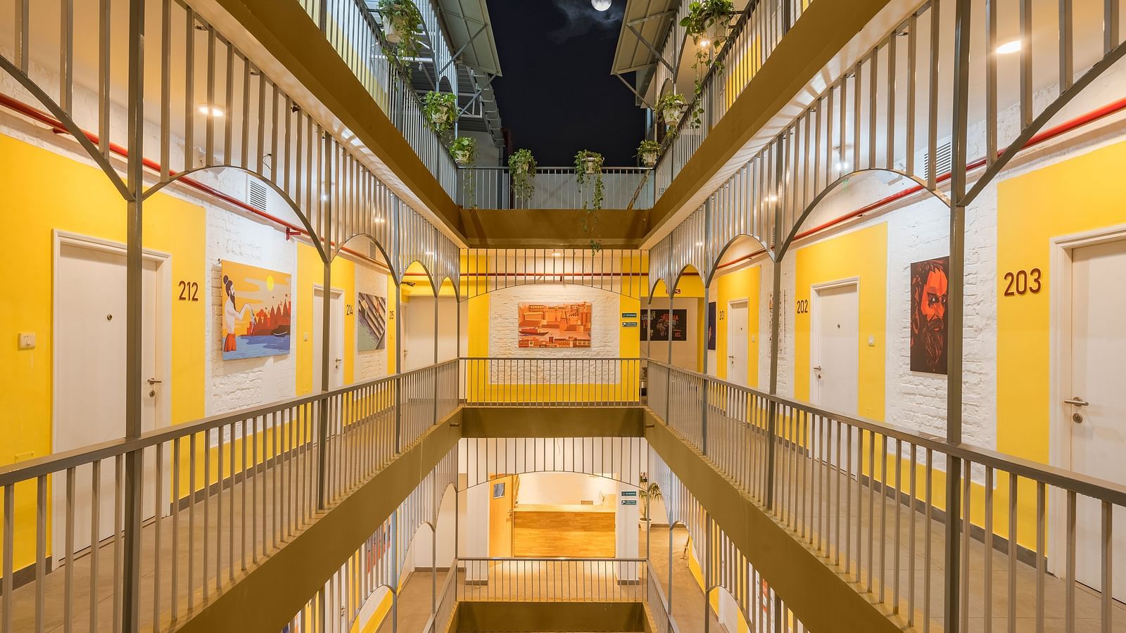 An image of the corridor at Bedzzz Varanasi, brightly lit, with a few wall paintings hanging on the walls, captured in the night.