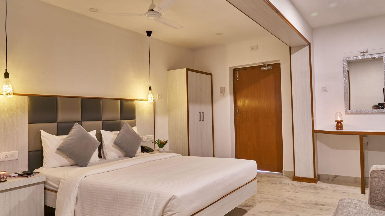 A bright and inviting hotel room at Hotel Mamallaa Heritage, featuring a bed with white linens, a bedside table, and an open doorway leading to another part of the room.