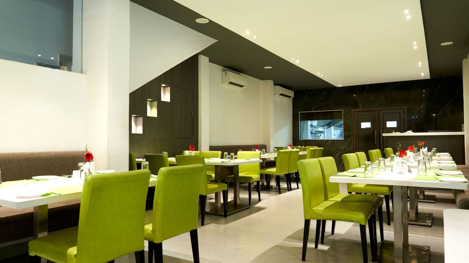 A spacious and contemporary restaurant area at Hotel Mamallaa Heritage, featuring multiple tables set with lime green chairs and white tablecloths.