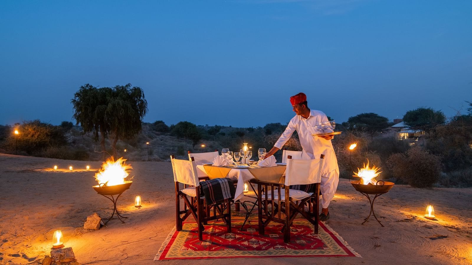 A man making an arrangement for the dinner in an outdoor setting with is decorated with lights - MANVAR Resort & Desert Camp