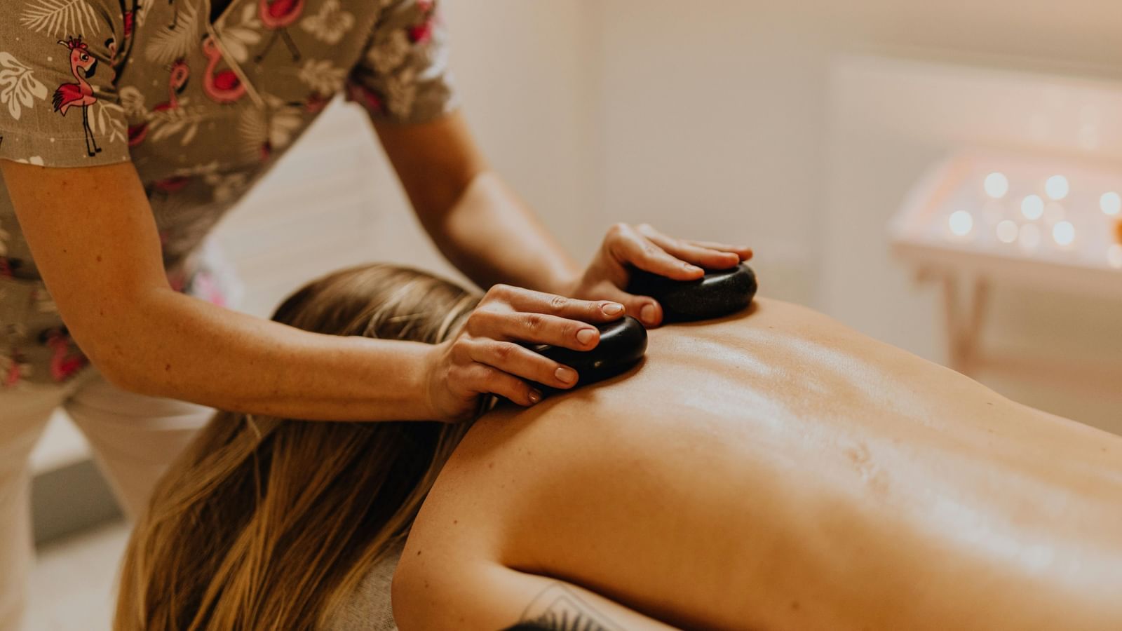Therapist giving a hot stone back massage to a woman lying on a spa bed in a relaxing setting.