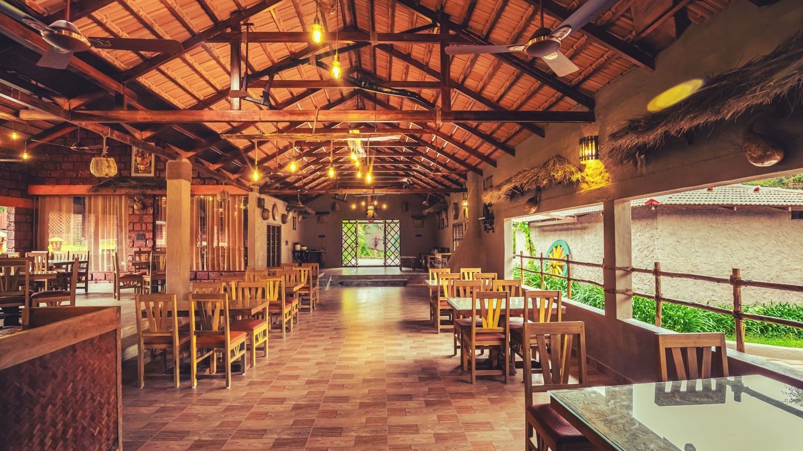 An interior shot of a spacious, open-air restaurant with a high wooden ceiling, many tables and chairs, and a view of the outdoors at The Copper Edge - Eco Resort, Coorg.