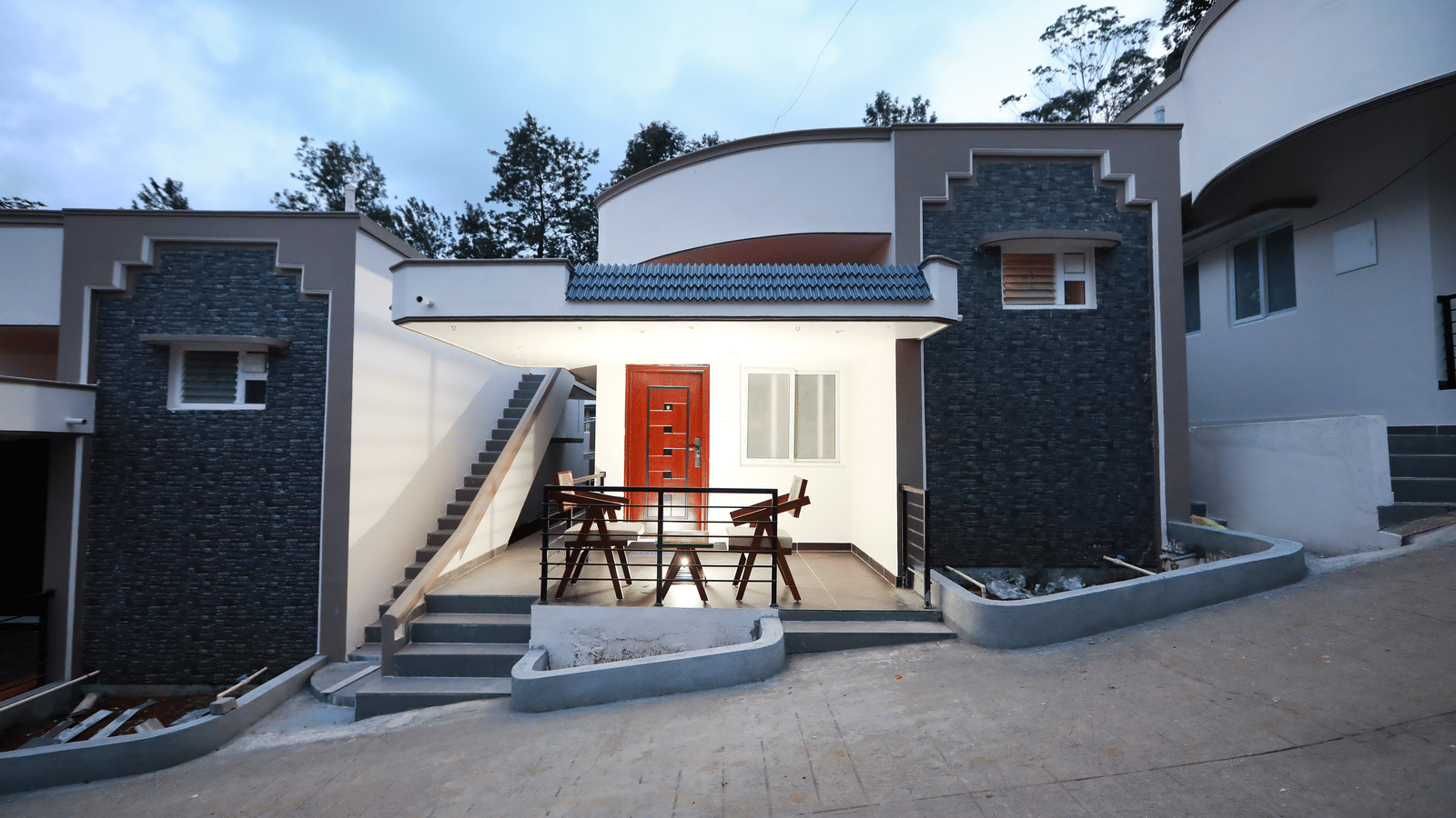 Front-view shot of the Nature Luxury Room exterior with the outdoor seating area lit up along with a cloudy sky in the background at WOW Naturefull Resorts, Yercaud.