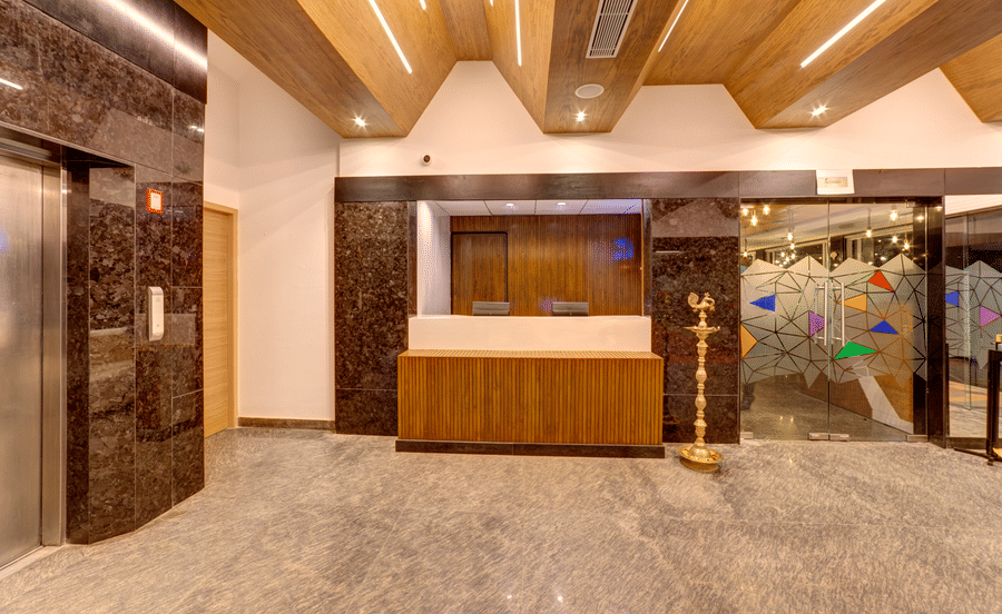 A wooden reception desk, an elevator, and a wooden slatted ceiling in the lobby of Icon Express By Bhagini, Mahadevapura.