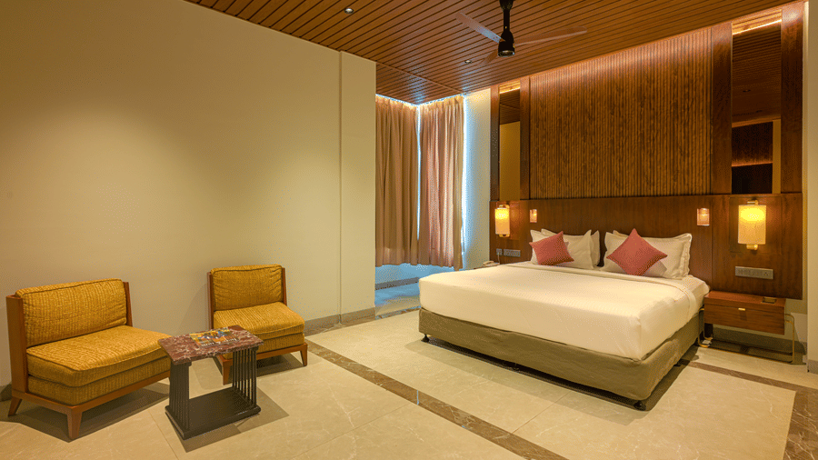 Spacious hotel bedroom with a king size bed, wooden ceiling, upholstered seating, bedside lighting and a large television.