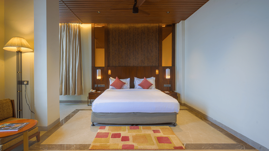 Hotel bedroom with a king size bed, patterned rug, wooden ceiling, bedside tables and warm ambient lighting.