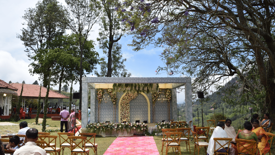 An outdoor wedding space at Ibex Resorts, Coonoor (Leewood), featuring wedding arrangements, and people seated with the trees in the backdrop.
