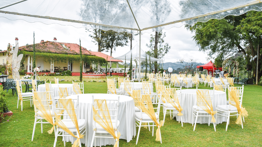 An outdoor wedding space at Ibex Resorts, Coonoor (Leewood), featuring chairs,  and tables placed under an umbrella.