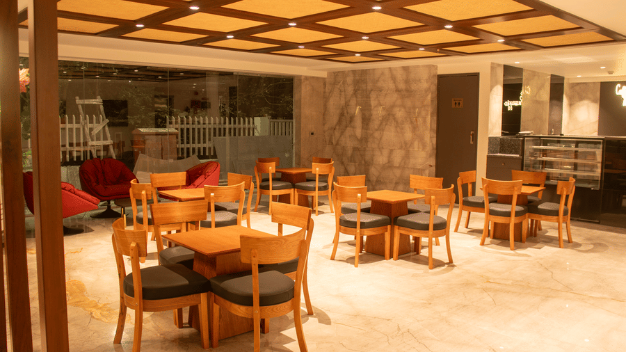 A hotel lobby area with wooden tables and chairs,  cushioned chairs, and ceiling lights arranged in a grid pattern.