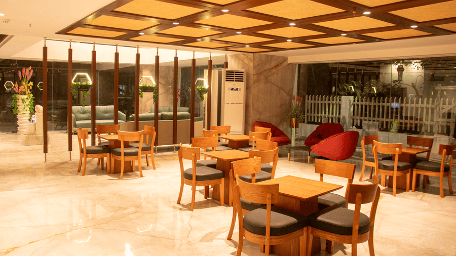 A hotel lobby area space with arranged tables and chairs, large windows, and patterned ceiling panels with lighting.