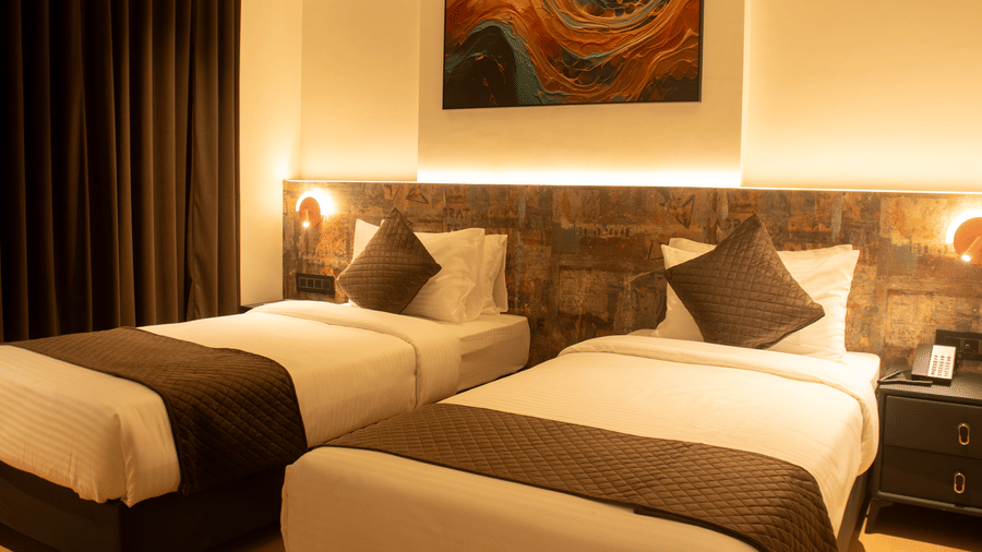 2 single beds room with bedside lamps, headboard panel, and wall art at Magnus Lxia Premier, Kalyani Nagar.