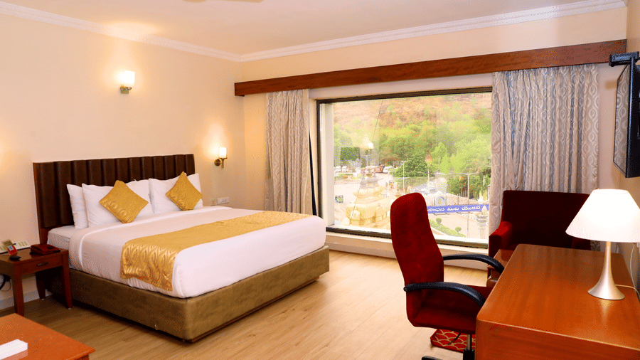 Hill View Room featuring a floor to ceiling window, a double bed, and desk and a chair inside Raj Park, one of the top hotels in Tirupati