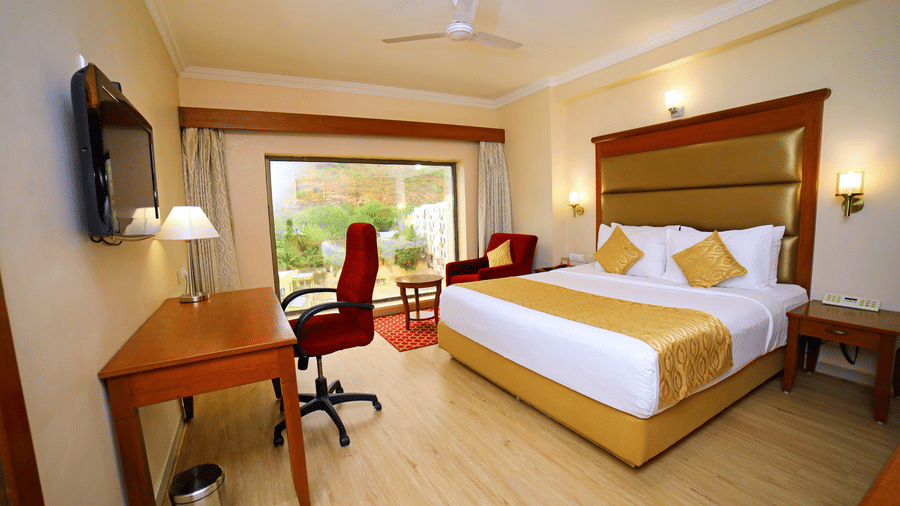 Hill View Room featuring a double bed facing a TV with a lamp on the work desk below, and a sofa next to the window at Raj Park Hotel, offering the best place to stay in Tirupati.